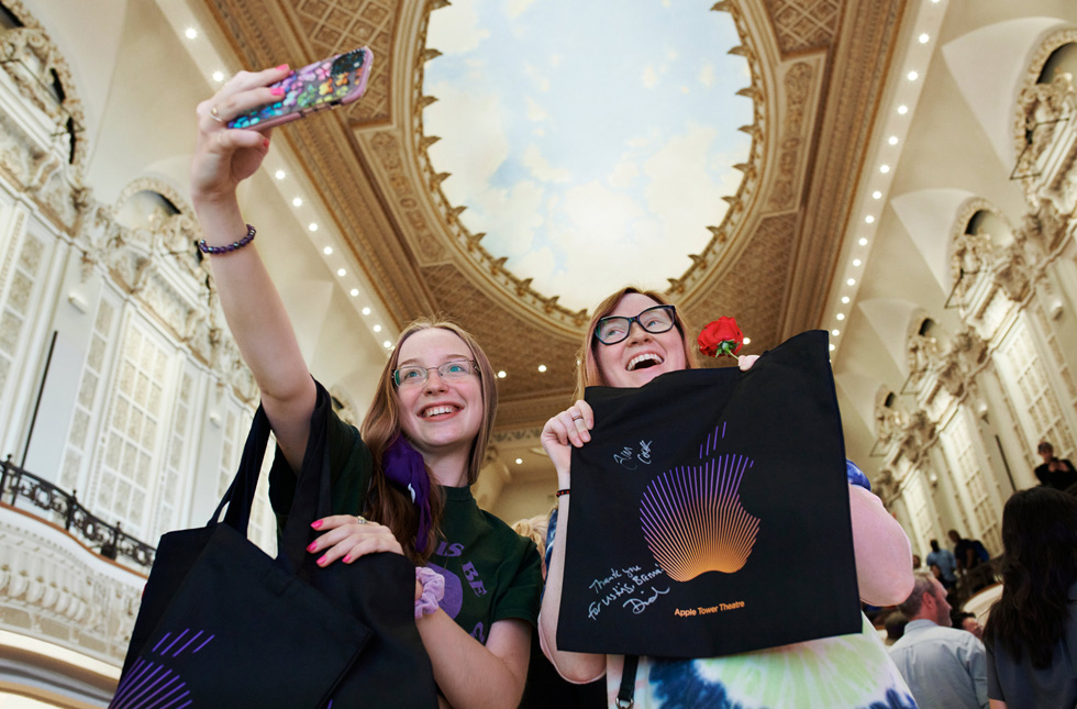 Due clienti si fanno un selfie con i loro acquisti Apple sotto la cupola dipinta come il cielo di Apple Tower Theatre.