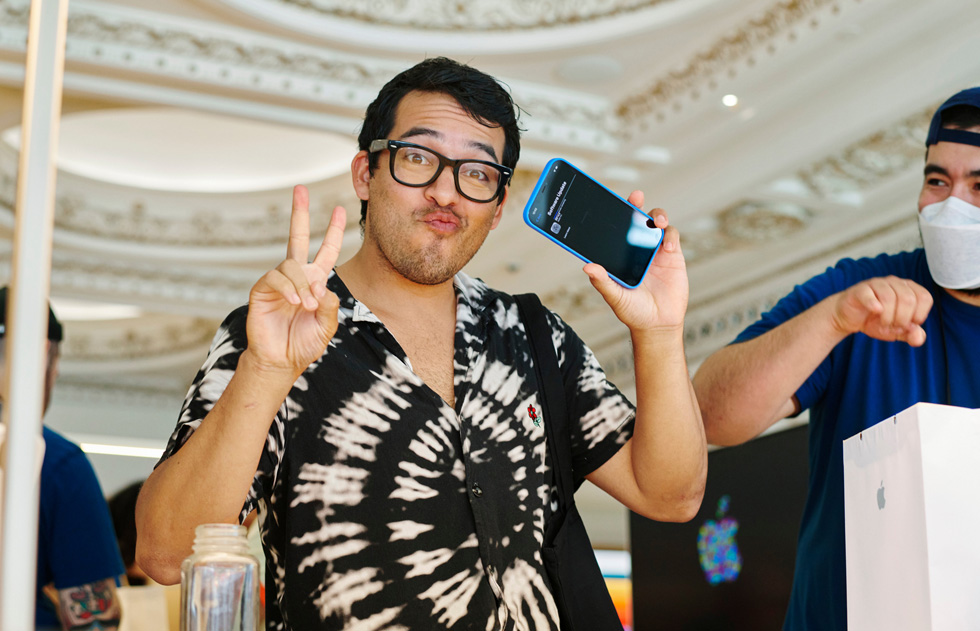 A customer flashes a peace sign with one hand and his iPhone 12 in another at Apple Tower Theatre.