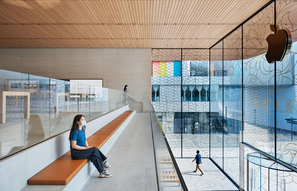 En Apple-medarbetare iförd munskydd sitter på en bänk i galleriet på ovanvåningen och blickar ut över torget.