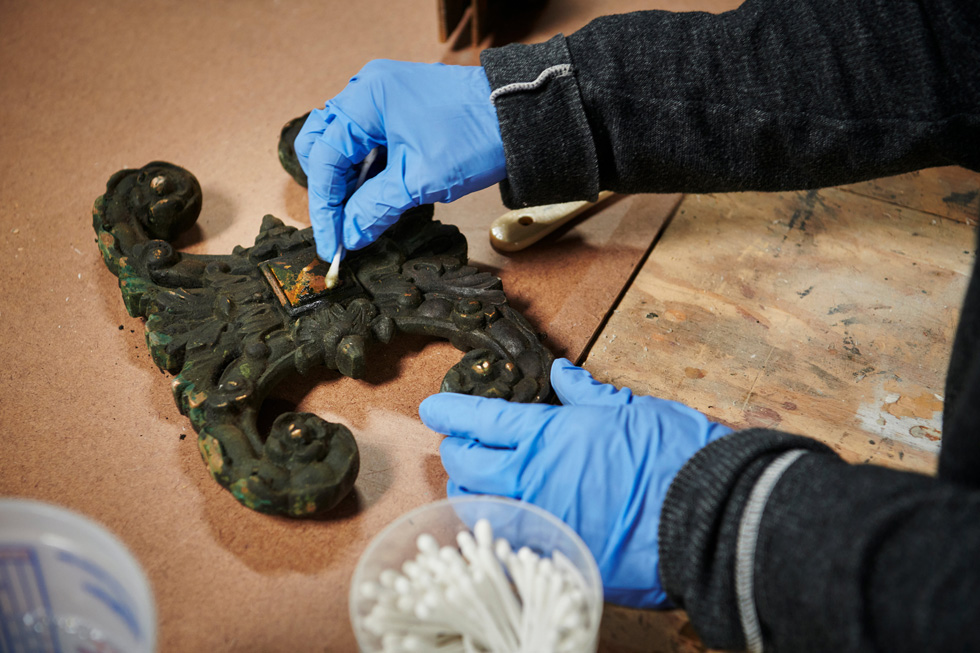 A decorative bronze piece is carefully restored to its original finish.