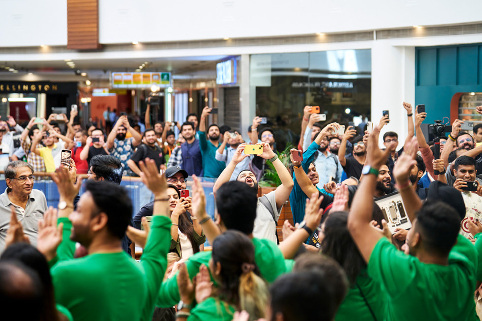 Un gruppo di clienti in fila all’esterno di Apple Saket, molti con le braccia alzate per scattare foto.