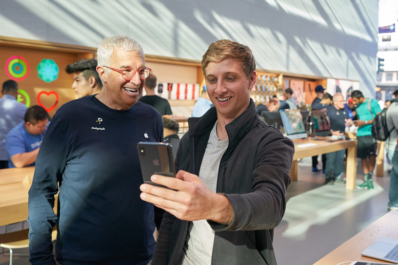 An Apple team member watches a customer take a selfie with an iPhone Xs.