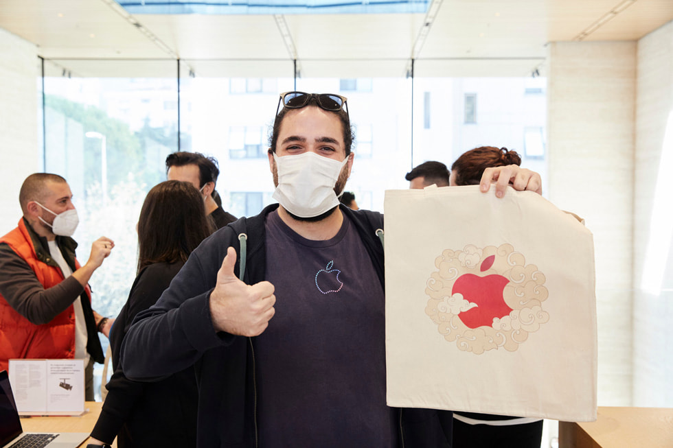 En mand iført en Apple T-shirt holder et billede af Apple-logoet og giver “thumbs up”.