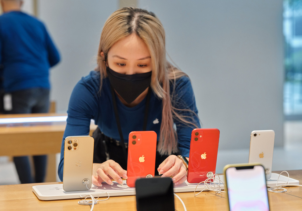 An Apple Orchard Road team member adjusts a display of iPhone SE, iPhone 11, iPhone 12, and iPhone 12 Pro.