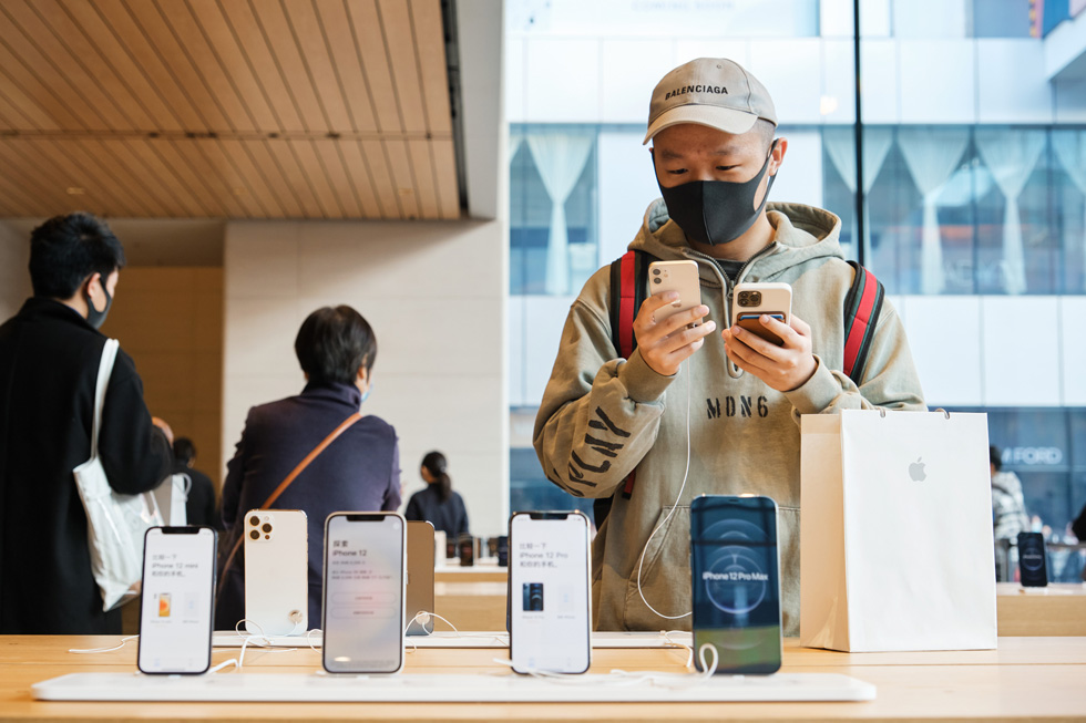 A customer at Apple Sanlitun closely examines iPhone 12 mini.