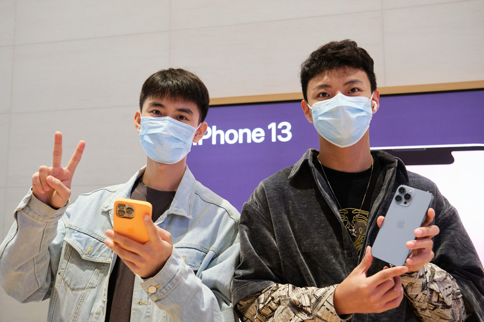 Ein Kunde mit einem Freund, der das neue Sierra Blue iPhone 13 Pro bei Apple Sanlitun hält.