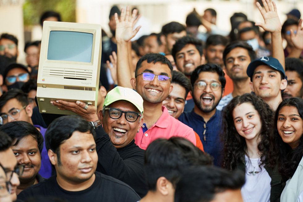 An excited customer waves an original Apple Macintosh personal computer in a sea of customers outside Apple BKC. 