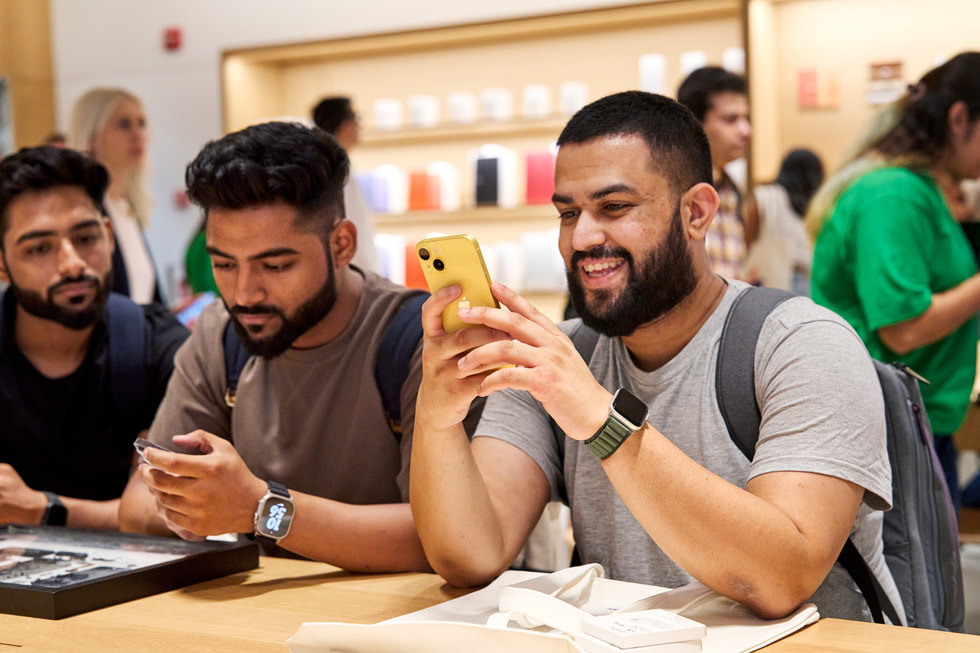 Ein Kunde sitzt an einem Tisch in Apple Saket und probiert das iPhone 14 im neuen Gelb aus.
