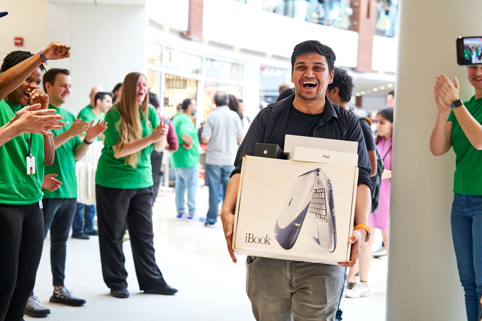 Teammitglieder schauen auf einen lachenden Kunden, der seine älteren Apple Produkte in den Armen hält.
