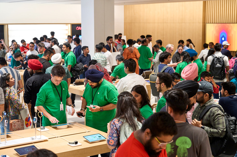 In Apple Saket unterhalten sich Kund:innen mit Teammitgliedern von Apple und stehen rund um die Tische, um mehr über die Vielzahl an dem im Store verfügbaren Geräten zu erfahren.
