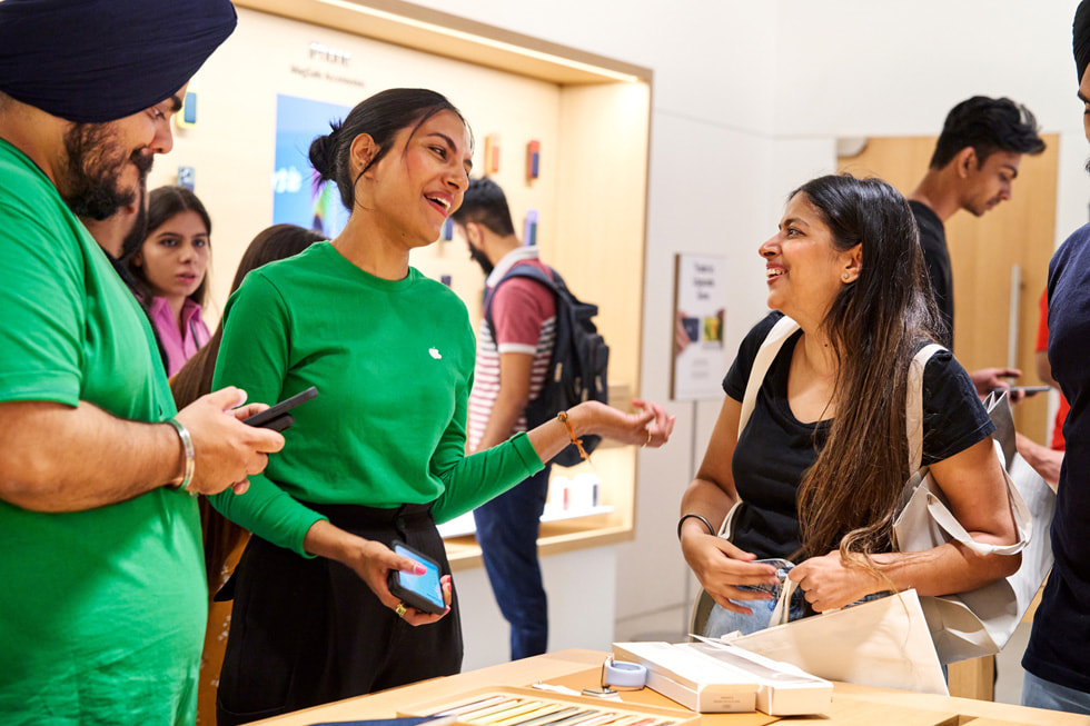 A smiling customer talks with two Apple team members.
