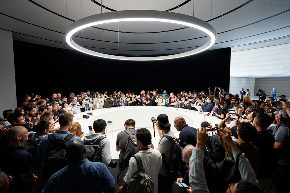Pressevertreter:innen stehen im Apple Park um ein Ausstellungsobjekt, das die Apple Vision Pro zeigt.