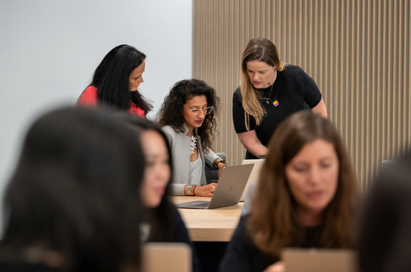 一台のMacBookの向こう側で二人のインストラクターと一緒に作業をする女性たち