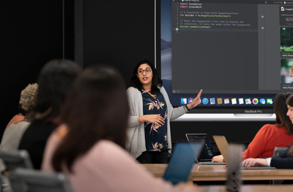 An instructor displaying coding on a MacBook Pro in front of a class of participants.