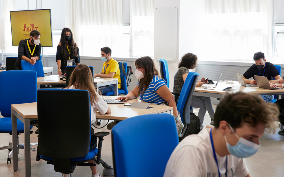 Estudiantes de la Developer Academy de Nápoles trabajan en varias mesas.