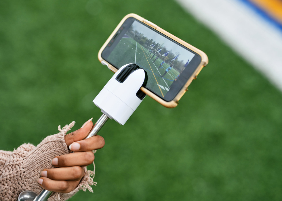 Een leerling van New Rochelle High School gebruikt een iPad om vlaggendragers te filmen op het sportveld.