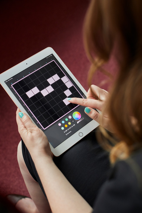 Un primer plano de una mujer usando la app imagiLabs para diseñar algo con cuadrados rosa sobre un fondo negro.