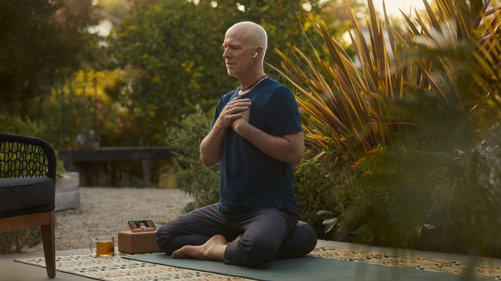 Uomo con gli AirPods che segue una sessione di yoga in Fitness+ su iPhone 14.