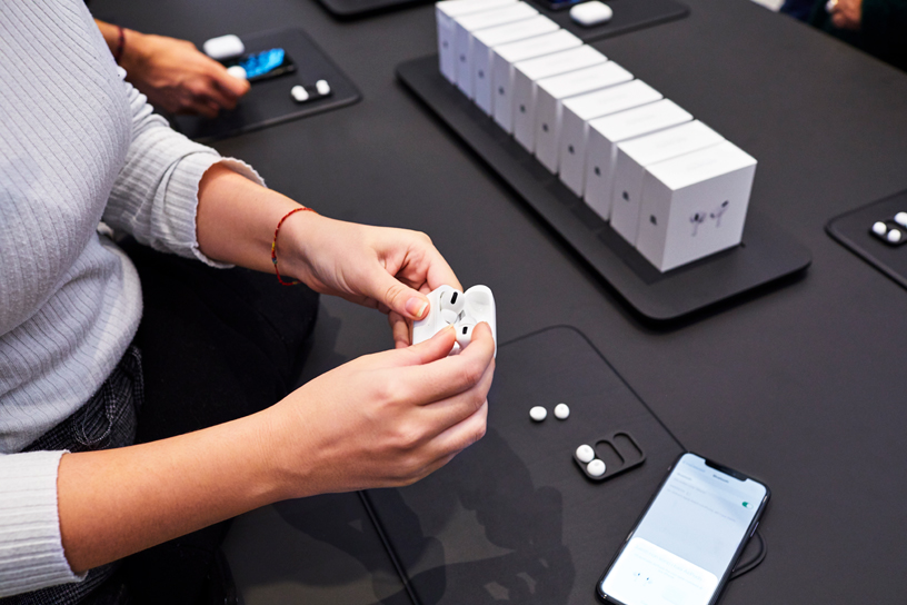 Une cliente ouvre le boîtier des AirPods Pro à une table à Apple Piazza Liberty à Milan.