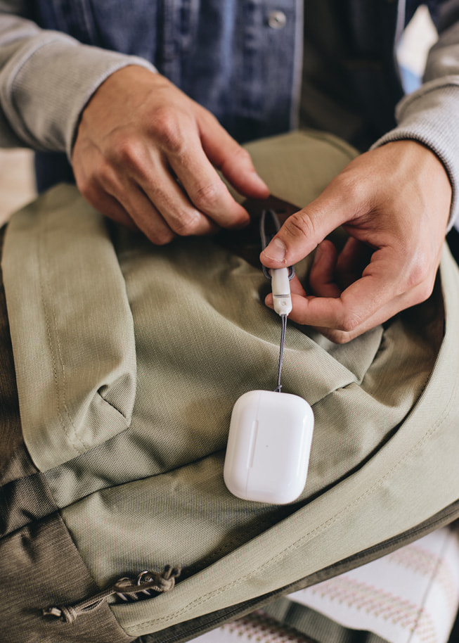 Lanyard mit Schlaufe hängt an einem Rucksack das am komplett neuen Case der AirPods Pro der zweiten Generation befestigt ist.
