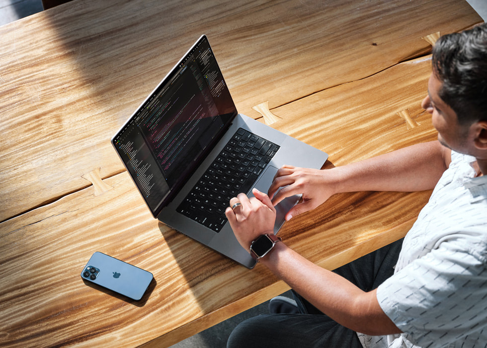 Une photo prise en plongée montre Swupnil Sahai utilisant un MacBook Pro à son bureau, avec un iPhone posé à côté.