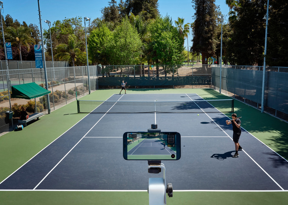 An iPhone is positioned to record two people playing tennis on a court.