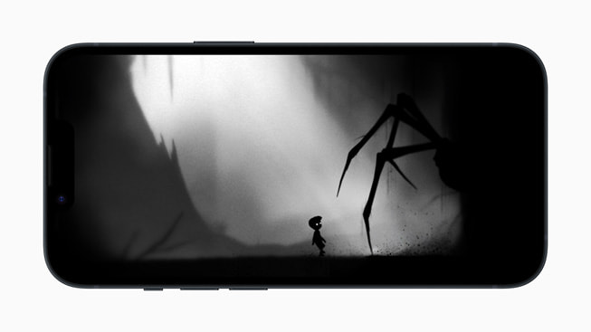 On iPhone 14, a still from the game Playdead’s LIMBO+ shows a giant spider lurking in the shadows near a small child.