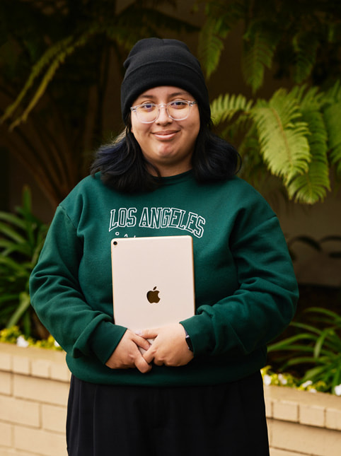 Retrato de Angela Ibarra, estudiante de Exceptional Minds. Angela lleva una sudadera verde con el texto «Los Angeles, California», gafas transparentes y una boina negra.