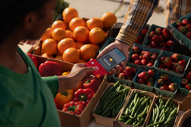 Seorang pelanggan menggunakan Tay to Pay di iPhone untuk membeli produk di pasar petani.