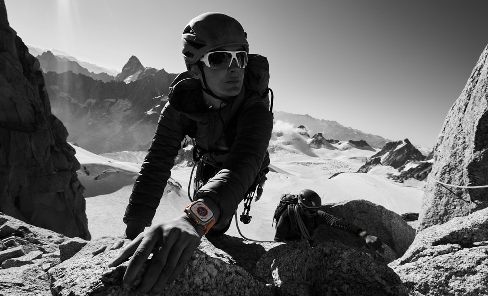 En person bruger Apple Watch Ultra, mens han klatrer på klipper i bjergomgivelser.