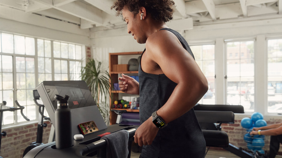 Donna con Apple Watch Series 8 e gli AirPods che segue un allenamento di tapis roulant Fitness+ su iPhone 14.