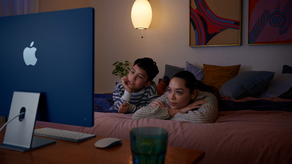 ベッドに寝そべって新しいiMacで番組を見ている女性と子ども。