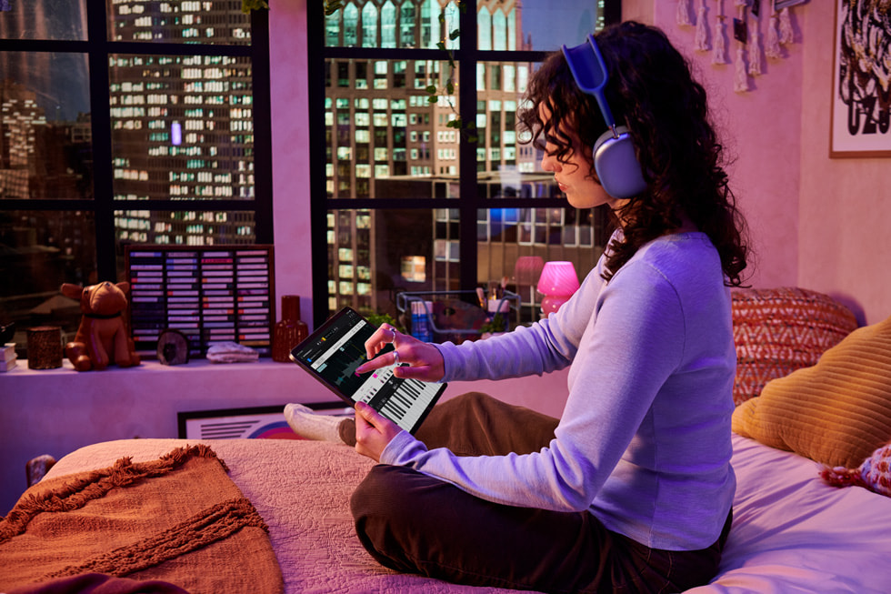 A person sitting on a bed in their high-rise apartment uses Logic Pro for iPad.