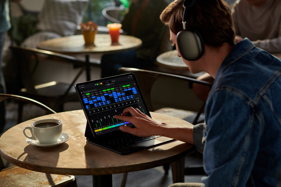 Pessoa com fones de ouvido usa o Logic Pro para iPad sentada a uma mesa com uma xícara de café.