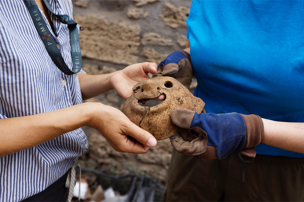 Two archaeologists hold a clay mask at the excavation site.
