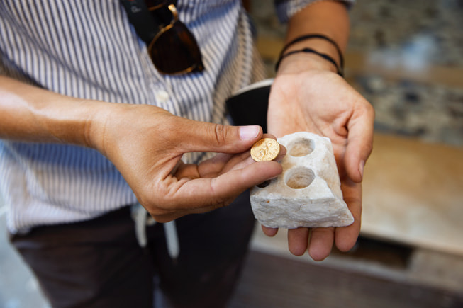 La Dra. Emmerson sostiene una moneda de oro en una mano y una roca con hoyos en forma de moneda en la otra mano