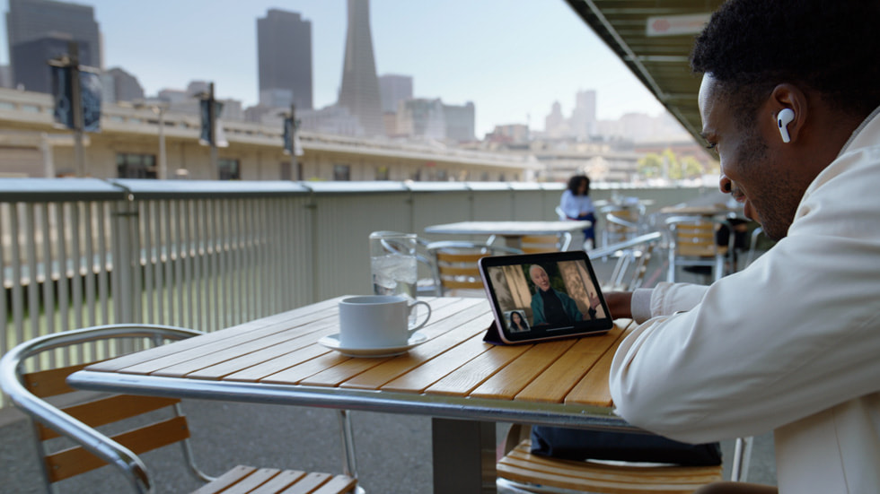 A person having coffee outside while using FaceTime and AirPods Pro with iPad mini.