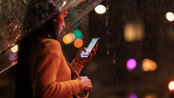 Mujer sosteniendo un paraguas y iPhone Xs en la lluvia.