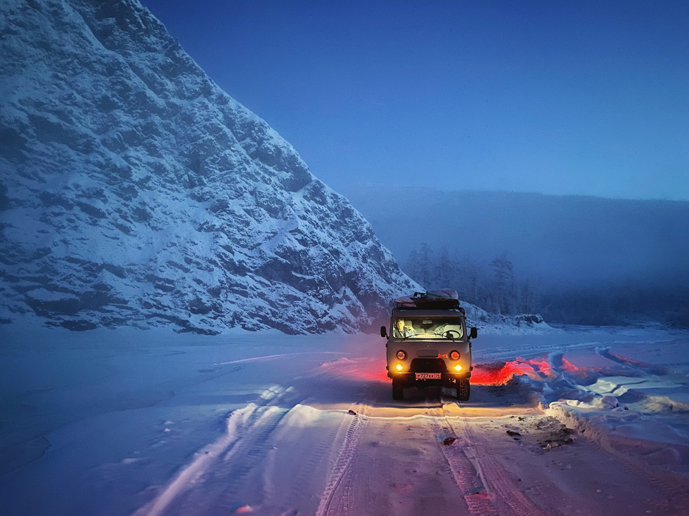 Bil på snødekt vei ved snøkledd fjell.