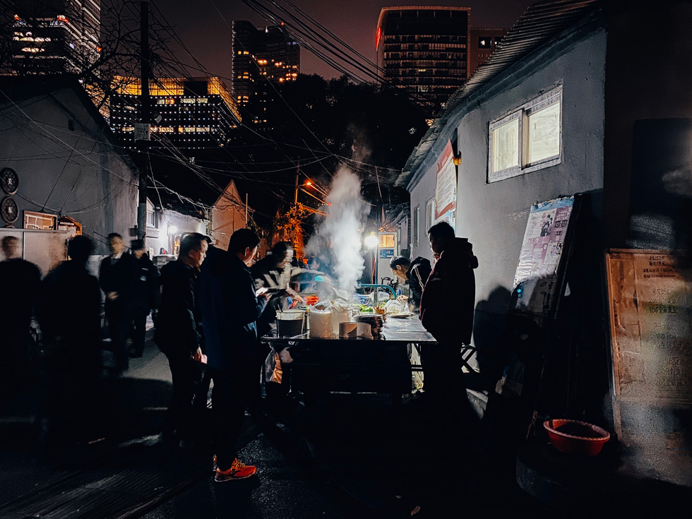 People on a dark street watching food being cooked.