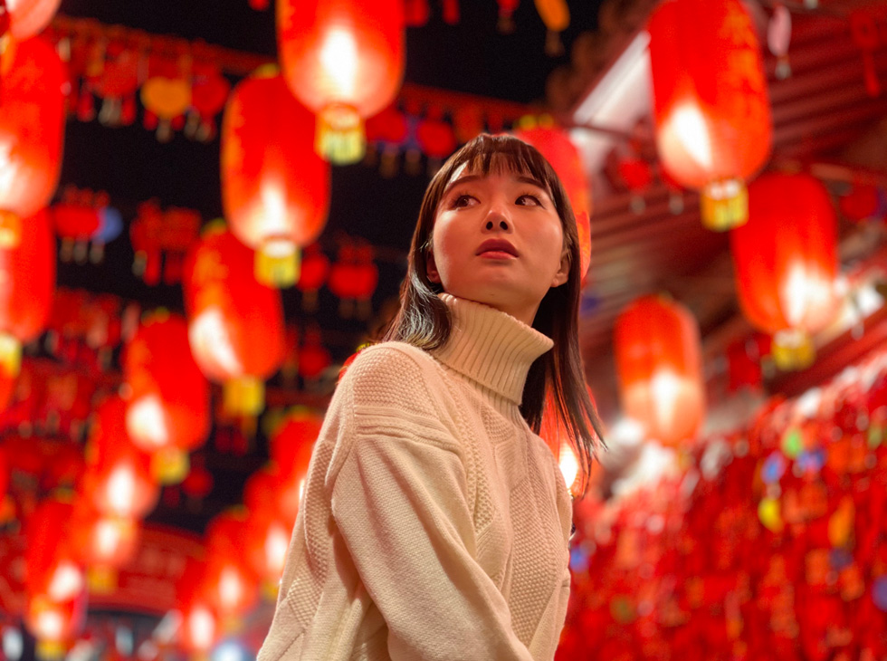 A woman photographed among glowing red paper lanterns strung overhead.