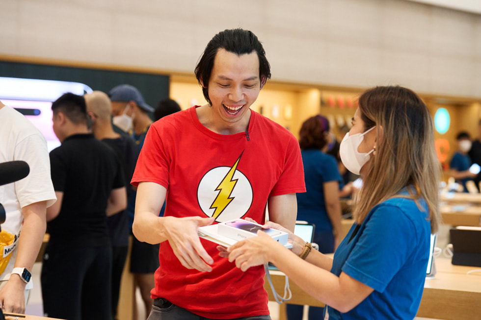 En Apple Orchard Road-kund ler medan han sträcker sig efter sin nya iPhone 14 Pro som en medarbetare håller i.