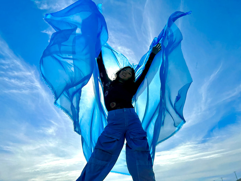 Une personne tient une écharpe bleue flottant sur un ciel azur.