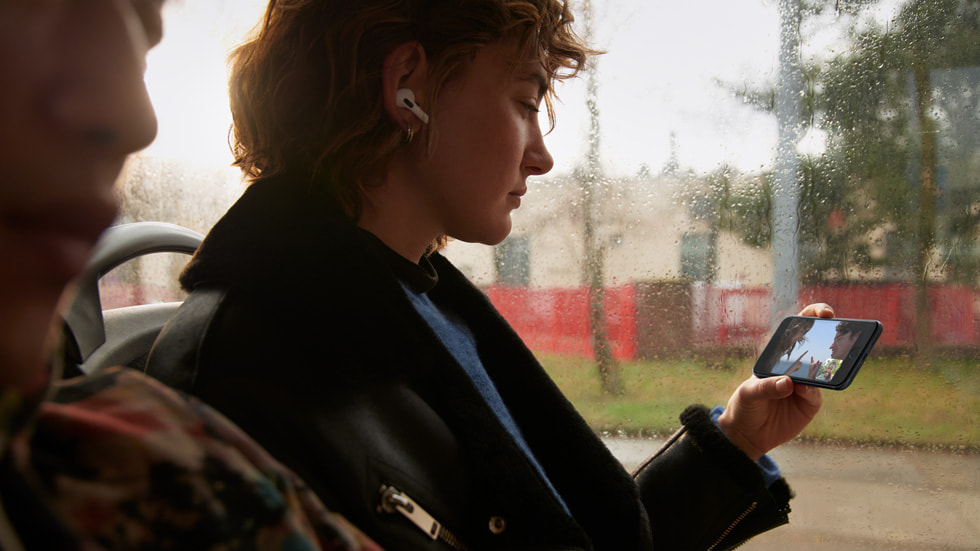Une personne portant des AirPods et regardant une vidéo dans un bus avec SharePlay sur un iPhone SE, grâce à la 5G.