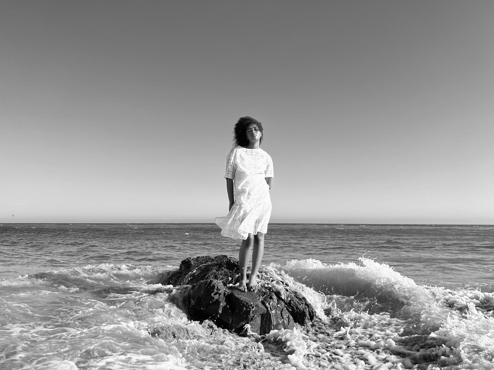 Woman standing by the ocean taken on iPhone 13 Pro’s Wide camera with sensor-shift OIS.