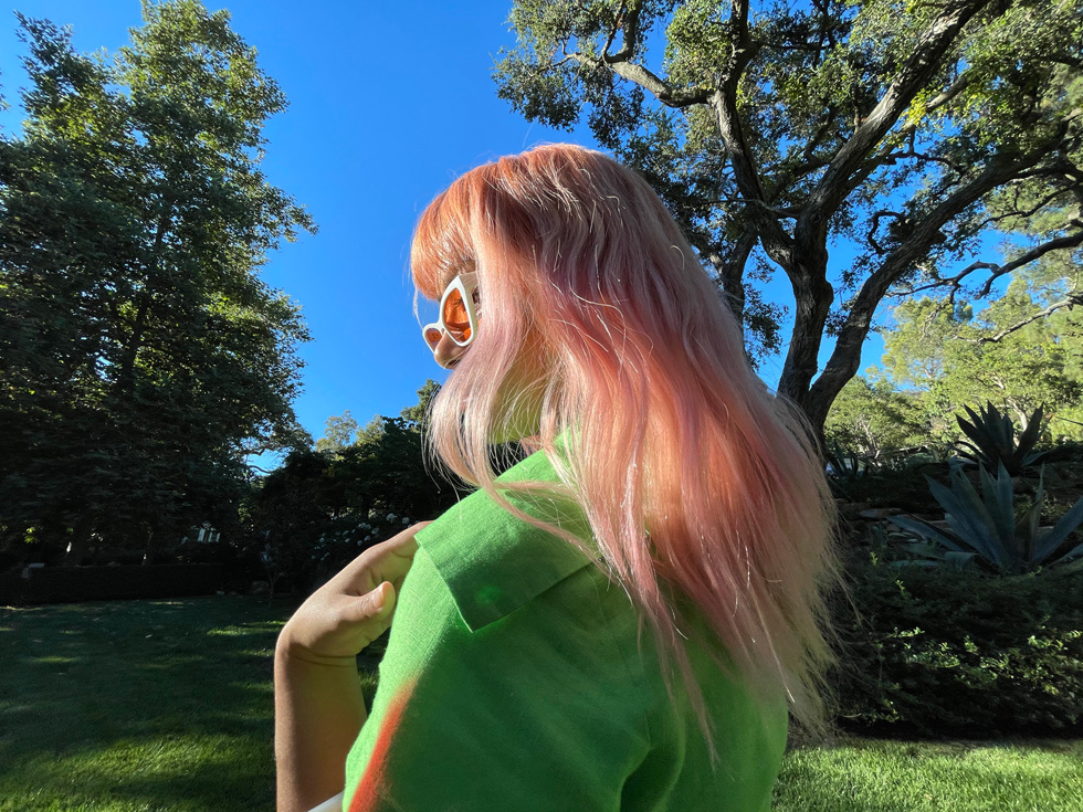 Porträtt av en kvinna med rosa hår taget med ultravidvinkelkameran på iPhone 12 Pro.