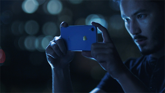 Un homme prenant une photo de nuit avec un iPhone Xr bleu.