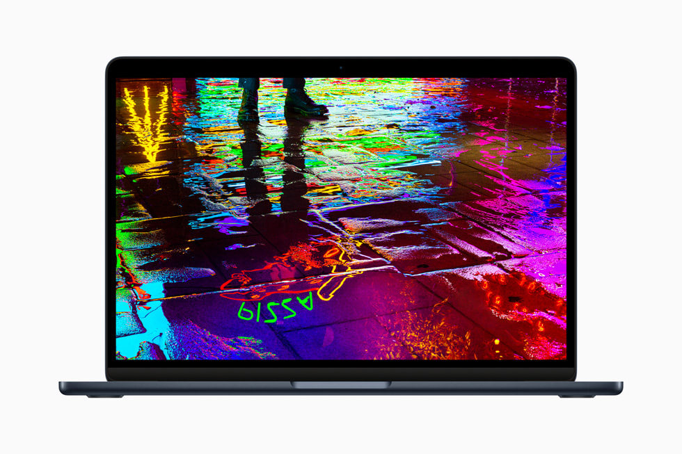  Une image montrant la lueur d’un néon se reflétant sur une chaussée humide s’affiche sur l’écran du nouveau MacBook Air avec puce M2. 