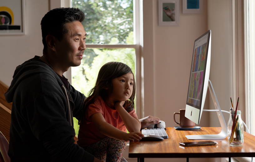 A father and daughter look at pictures on an iMac in their home.