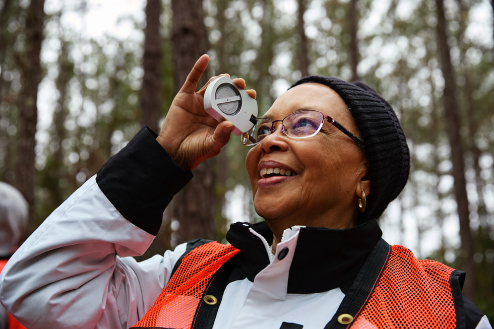 A woman holds a measuring device up to her eye in the community forest.